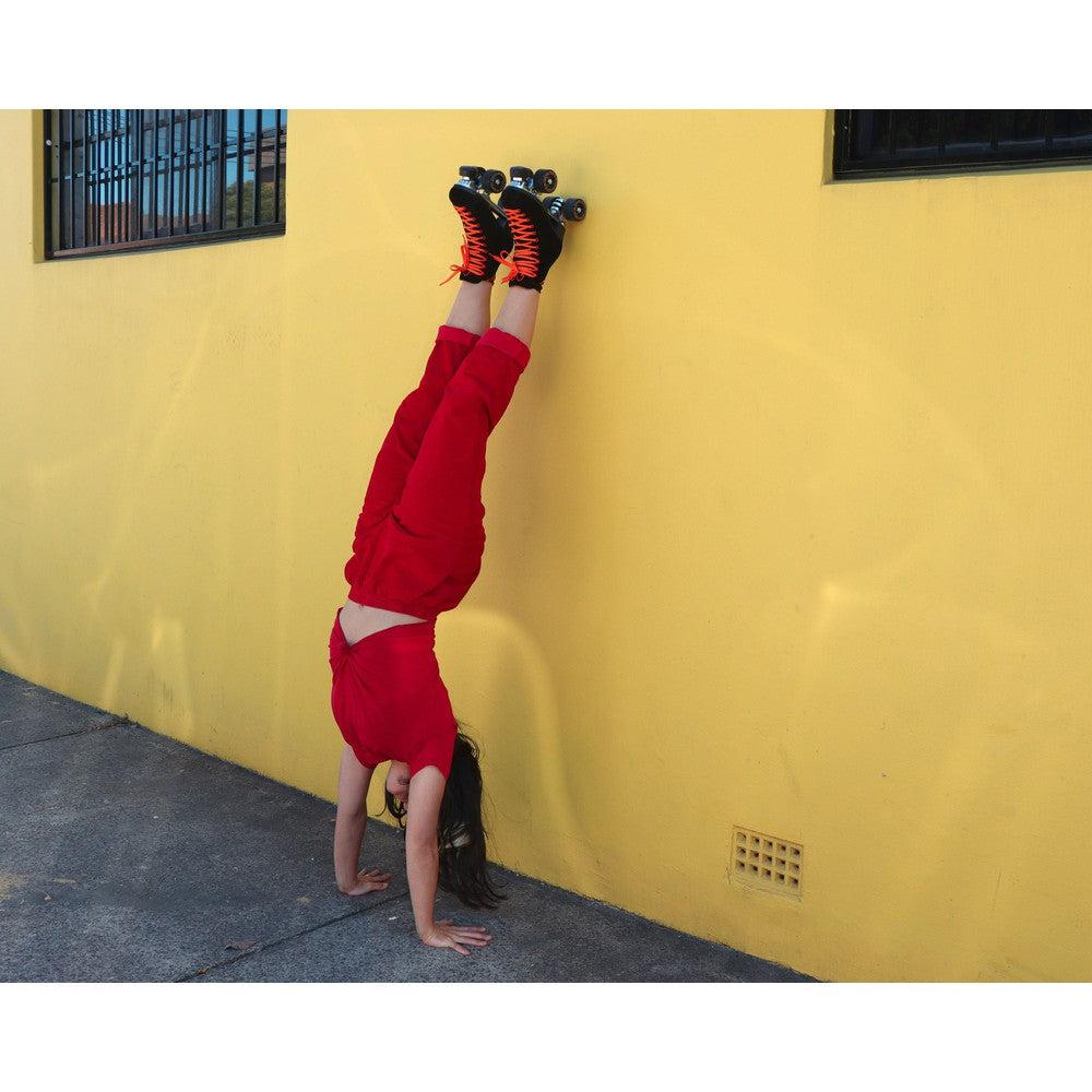 rollerskater doing a handstand wearing Chuffed Skates black roller skates on yellow wall